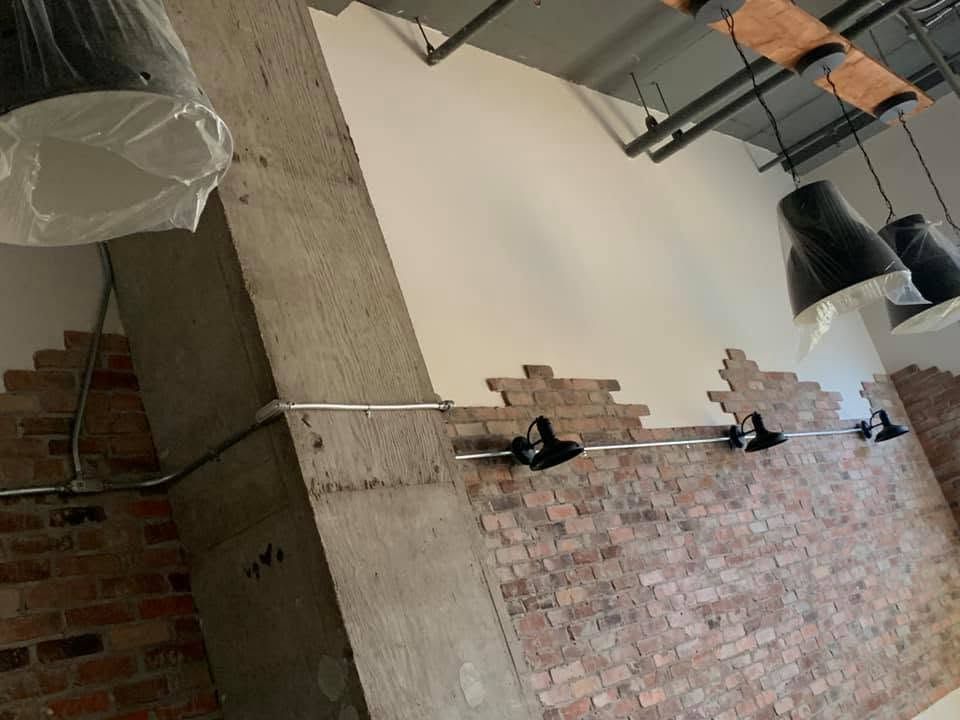Un mur de brique avec projecteurs noirs et conduit apparent, avant les finitions