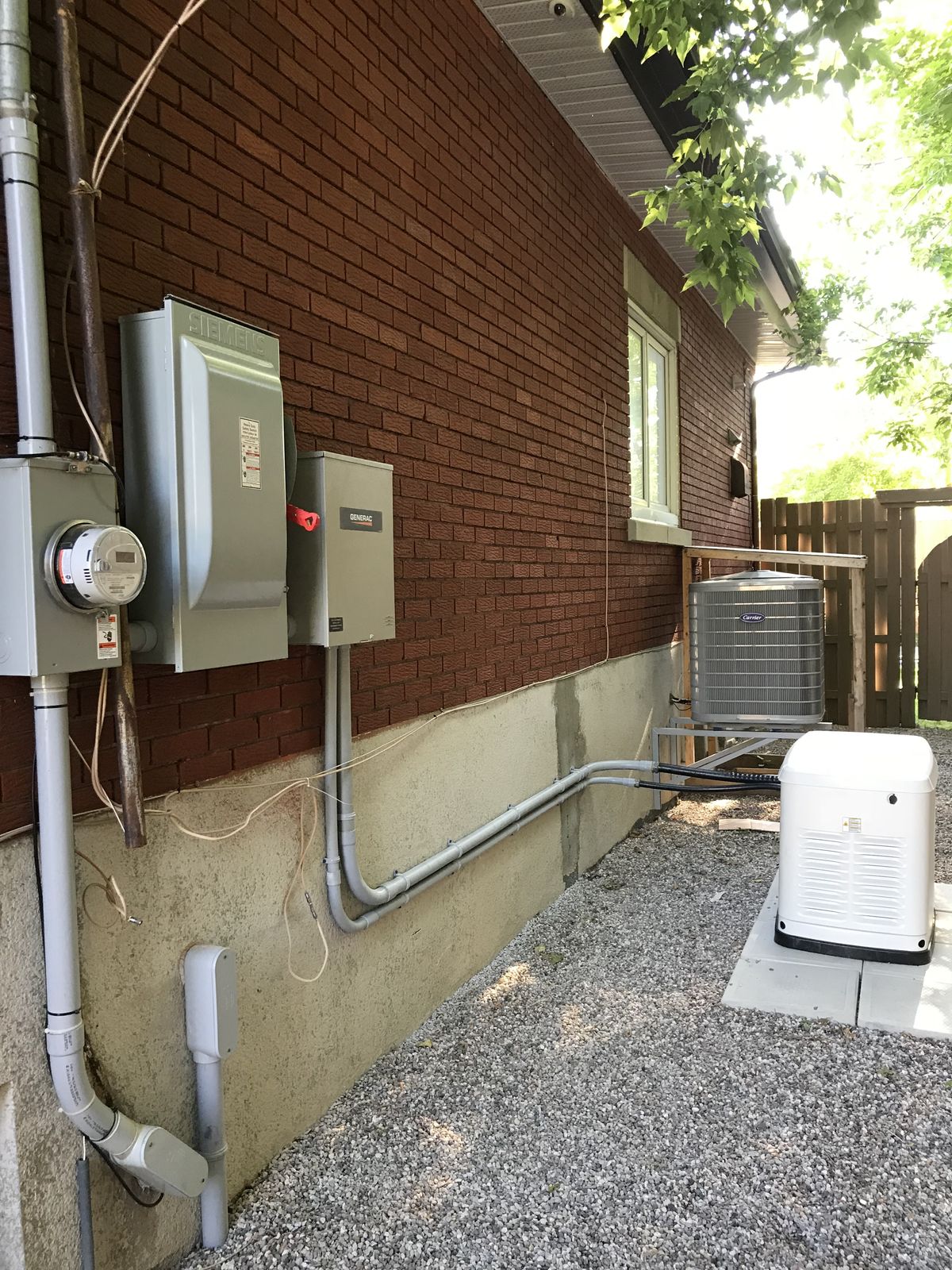 A standby generator installed beside a brick home, wired to a transfer switch with tidy conduit